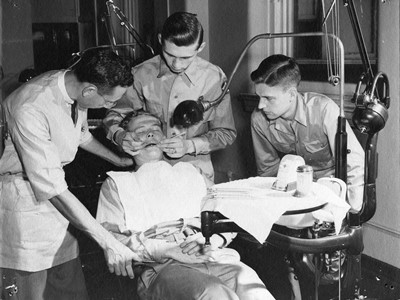 Студенты V-12 Луисвилльского университета проводят стоматологический осмотр пациента, ок. 1943 г. Фото взято с фотовыставки колледжа гуманитарных и естественных наук, посвященной программе военной подготовки офицеров, архив Луисвилльского университета.