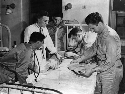 University of Louisville V-12 participants at patient's bedside, circa 1943. From the College of Arts & Sciences V-12 photo display, University of Louisville Archives & Special Collections.
