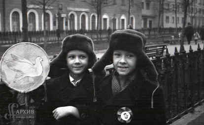Двое школьников в шапках-ушанках с транспарантом «Голубь мира» на демонстрации [7 ноября] на Комсомольском проспекте в городе Перми в. 1959 г.  АГП. Ф. 1053. Оп. 4. Д. 17.